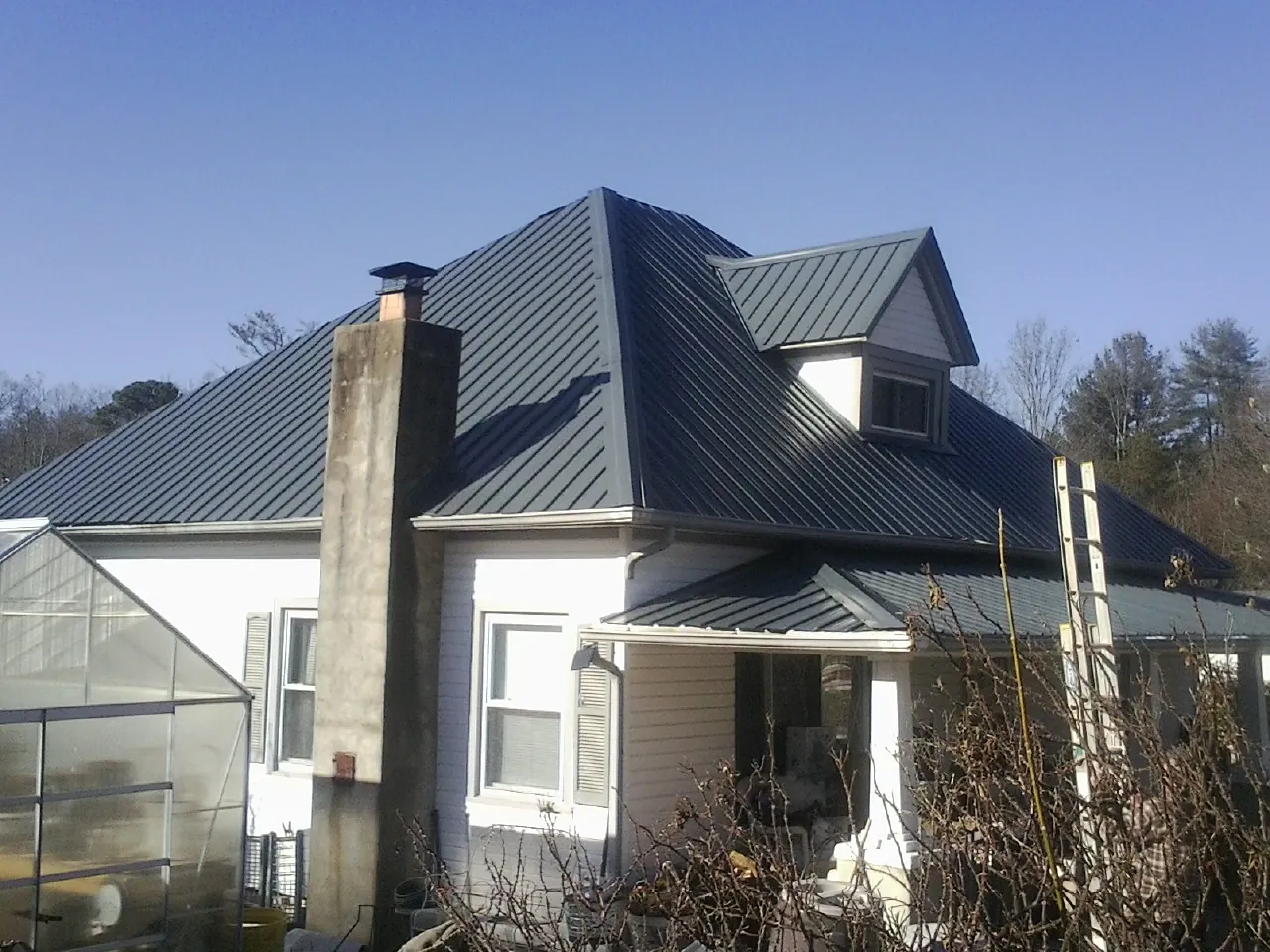 Dark blue standing seam metal roof on a white farmhouse with dormer — Slate & Tile Roof Repair by Roofing Brothers in Manistee