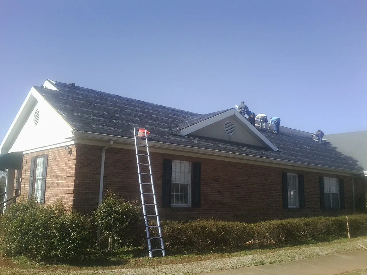 Crew tearing shingles off a brick ranch roof with a ladder set — Emergency Roof Repair work by our crew in Manistee