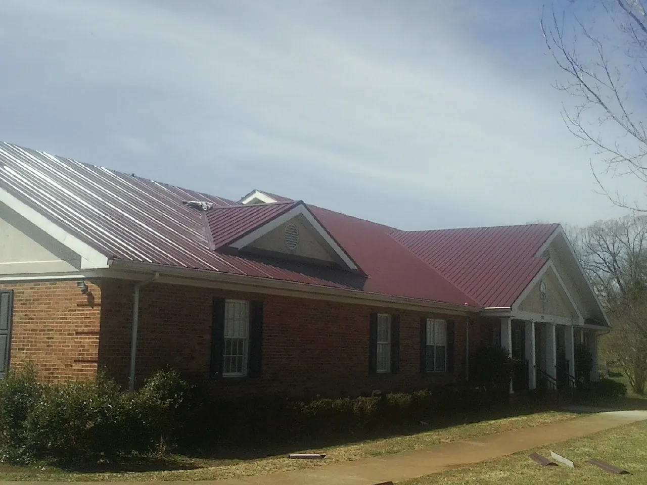 Red metal roof with gabled entries on a long brick building, from a Hail Damage Roof Repair job in Manistee