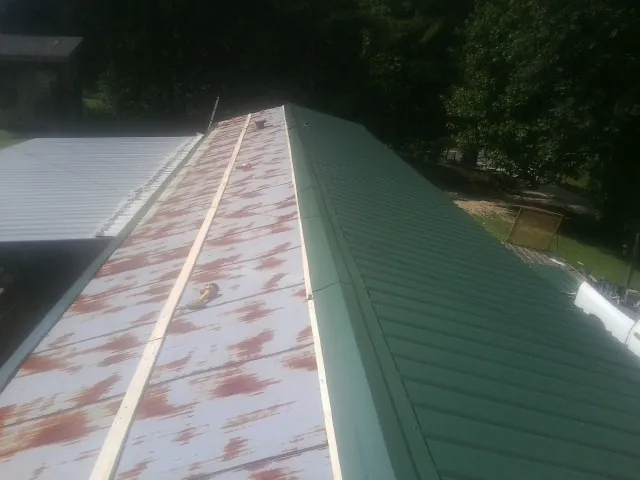 Old rusted panels beside newly installed green metal roofing — Wind Damage Roof Repair by Roofing Brothers in Manistee