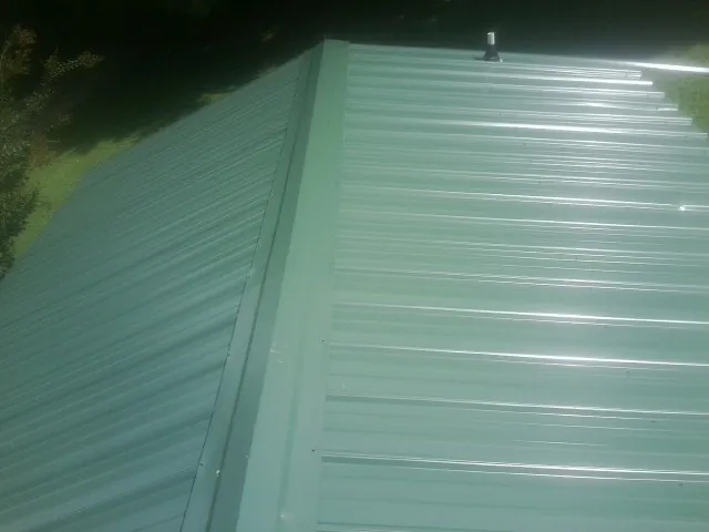New green metal panels meeting at the ridge of a roof — Flat Roof Repair work by our crew in Manistee