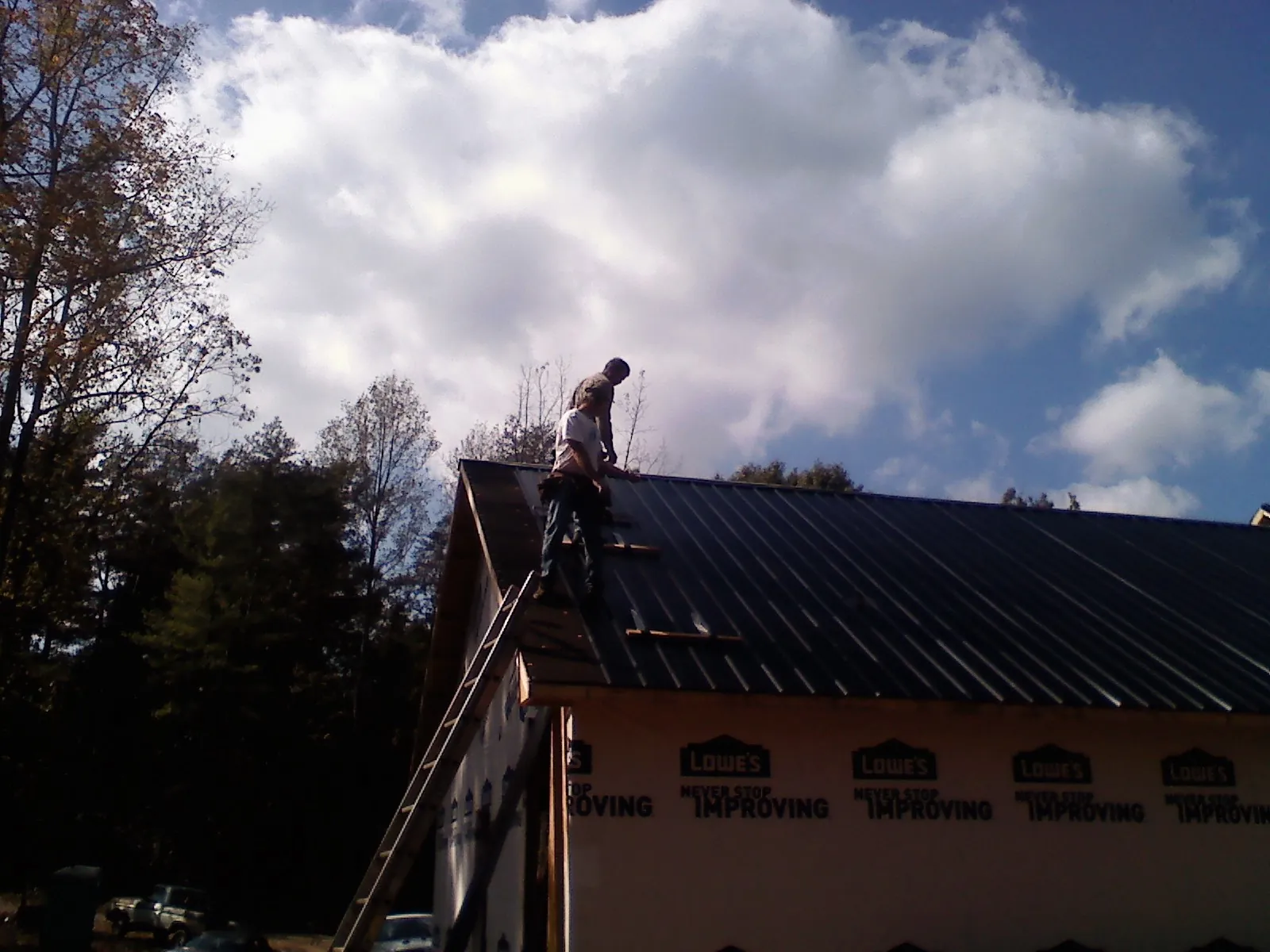 Roofer fastening dark metal panels high against a cloudy sky, from a Roof Inspection job in Manistee