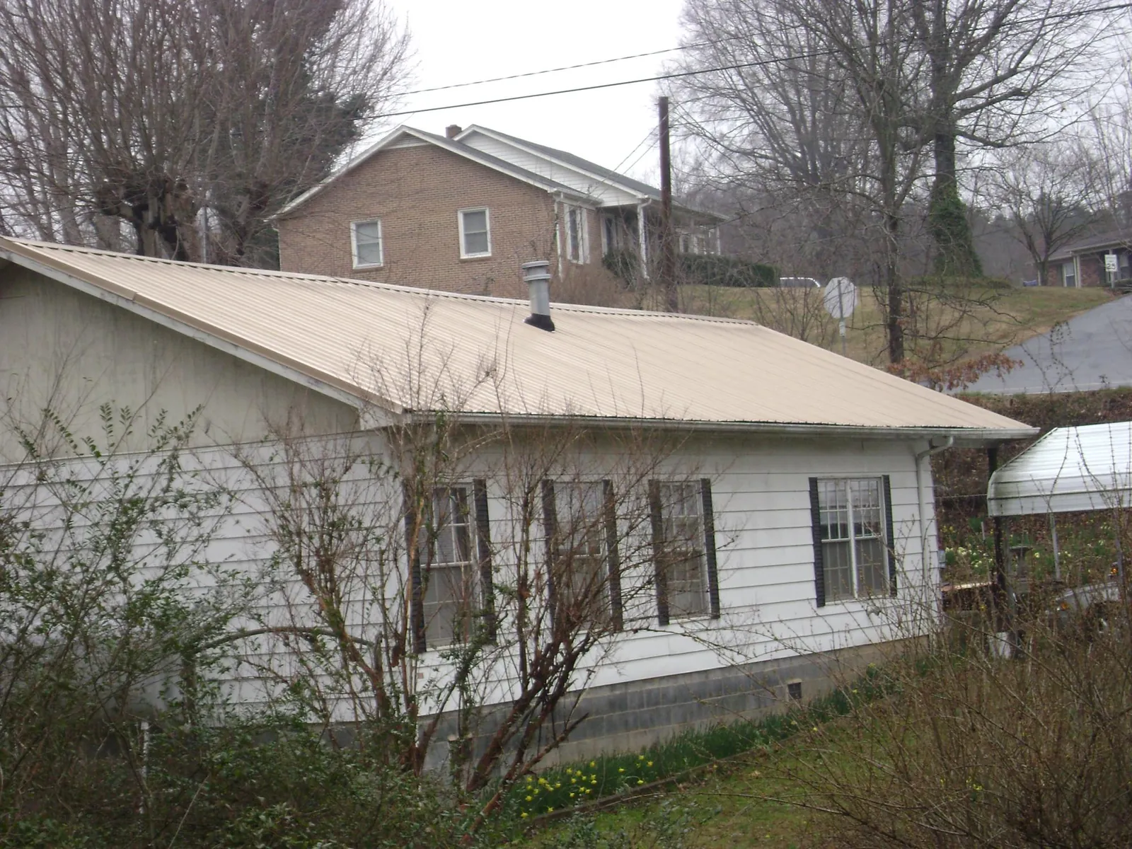 Tan metal roof on a white sided house set into a hillside — Commercial Roofing by Roofing Brothers in Manistee