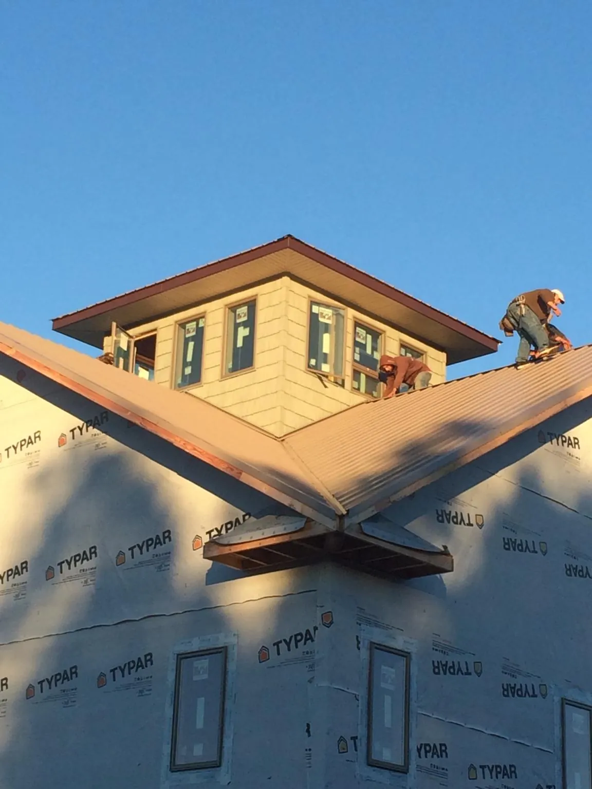 Roofers working around a rooftop cupola on a new metal roof at sunset — Roof Waterproofing in Manistee by Roofing Brothers